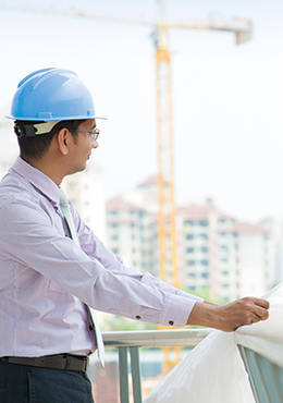 Bauleiter auf einer Großbaustelle mit Bauplan in der Hand und einem Baukran im Hintergrund